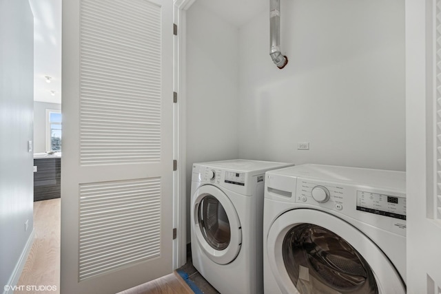 clothes washing area with washer and clothes dryer and light wood-type flooring