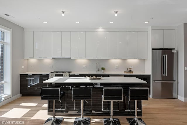 kitchen featuring a breakfast bar area, stainless steel refrigerator, sink, and white cabinets