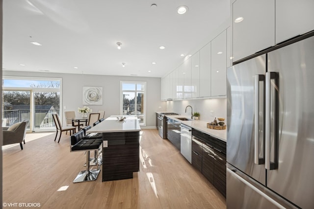 kitchen featuring appliances with stainless steel finishes, a breakfast bar, sink, light hardwood / wood-style flooring, and white cabinets