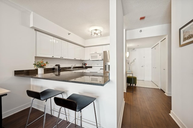 kitchen with kitchen peninsula, dark hardwood / wood-style flooring, a textured ceiling, white appliances, and white cabinetry