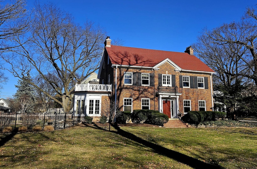 colonial home with a balcony and a front lawn