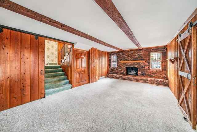 unfurnished living room featuring a fireplace, beam ceiling, carpet, and wood walls