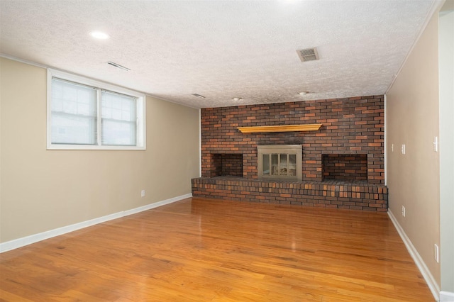 unfurnished living room featuring wood-type flooring, a textured ceiling, and a brick fireplace