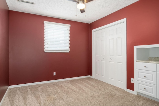 unfurnished bedroom featuring carpet flooring, a textured ceiling, a closet, and ceiling fan