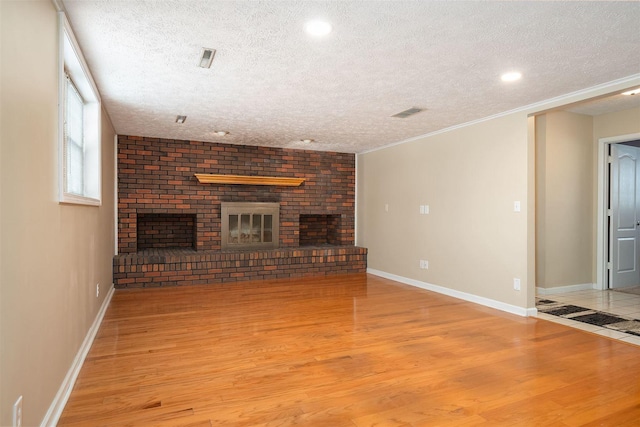 unfurnished living room with a textured ceiling, light wood-type flooring, a brick fireplace, and ornamental molding