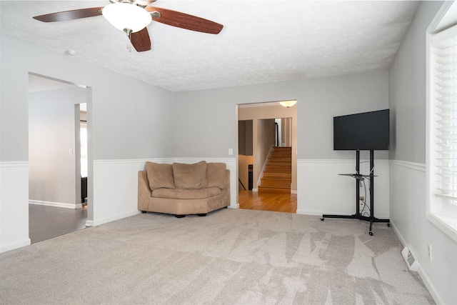 living room with ceiling fan, carpet floors, and a textured ceiling