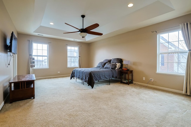 bedroom featuring multiple windows, light carpet, a tray ceiling, and ceiling fan