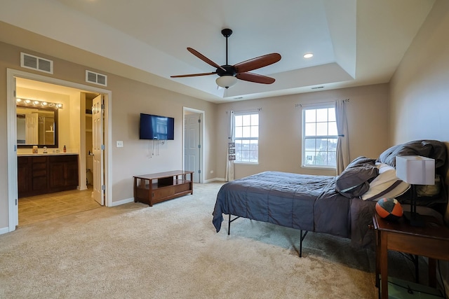 carpeted bedroom featuring ceiling fan, connected bathroom, and a tray ceiling