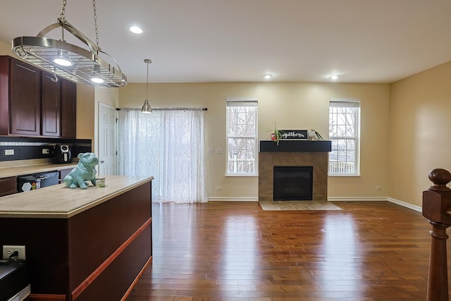 kitchen featuring pendant lighting, a center island, dark wood-type flooring, black dishwasher, and a tiled fireplace