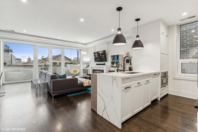 kitchen featuring sink, dark wood-type flooring, light stone counters, decorative light fixtures, and white cabinets