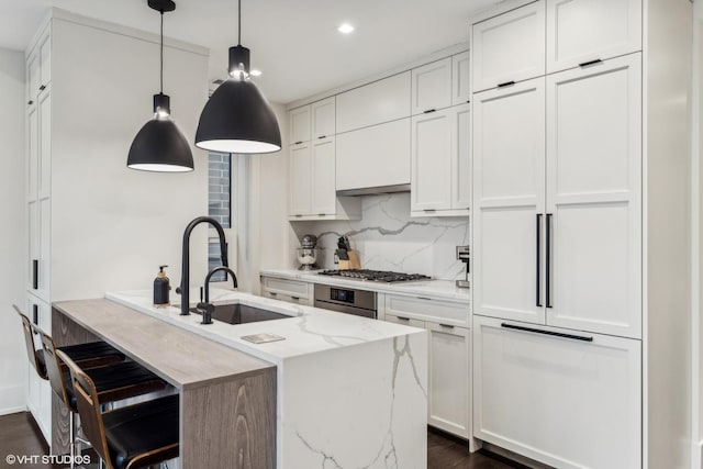 kitchen featuring a kitchen island with sink, white cabinetry, light stone counters, and decorative light fixtures