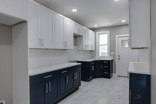 kitchen with blue cabinetry, decorative backsplash, sink, and white cabinets