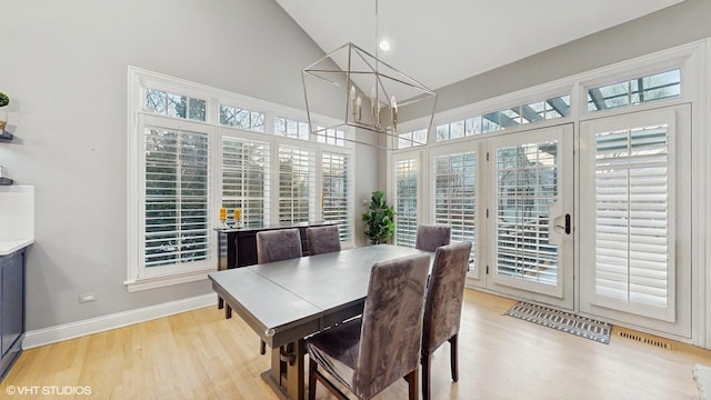 dining area featuring wood-type flooring, high vaulted ceiling, and an inviting chandelier