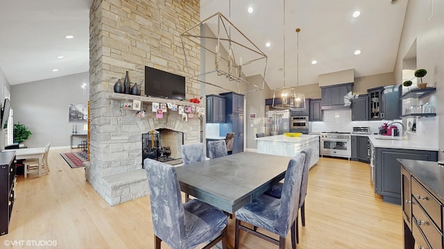 dining room featuring light hardwood / wood-style floors, high vaulted ceiling, a stone fireplace, and sink