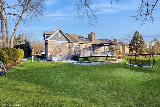 rear view of property with a yard, a trampoline, and a deck