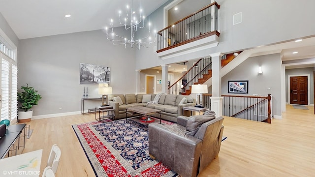 living room with ornate columns, a towering ceiling, an inviting chandelier, and light wood-type flooring