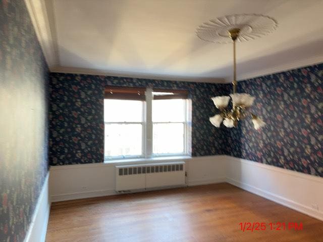 spare room featuring light wood-type flooring, a chandelier, and radiator