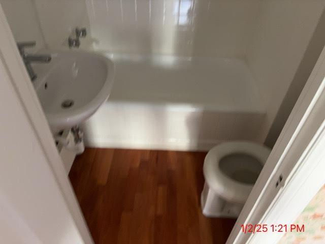 bathroom with sink, a washtub, toilet, and wood-type flooring