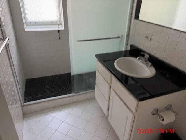 bathroom with tile walls, tile patterned flooring, a shower with door, and vanity