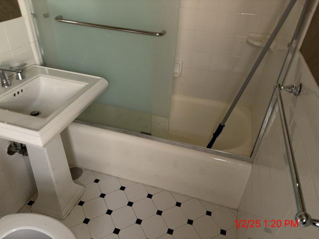 bathroom featuring toilet and bath / shower combo with glass door