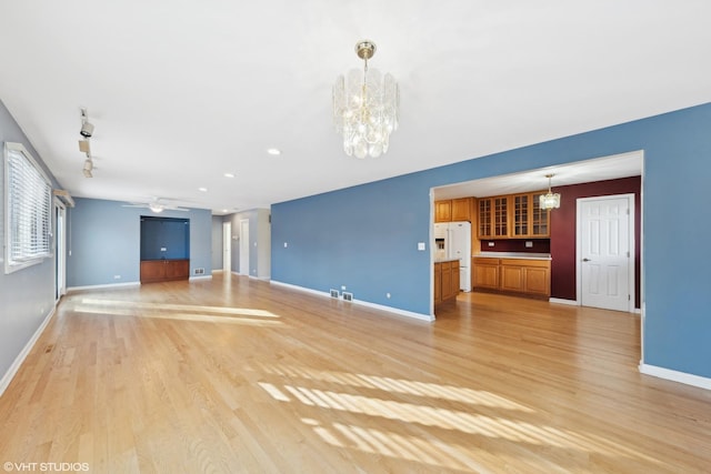 unfurnished living room featuring ceiling fan with notable chandelier, light hardwood / wood-style flooring, and track lighting