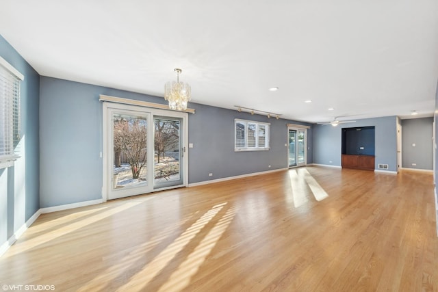 unfurnished living room featuring ceiling fan with notable chandelier and light wood-type flooring