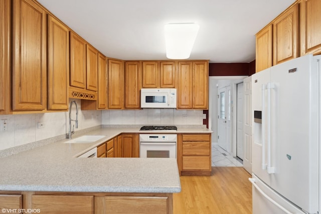 kitchen with kitchen peninsula, light wood-type flooring, tasteful backsplash, white appliances, and sink