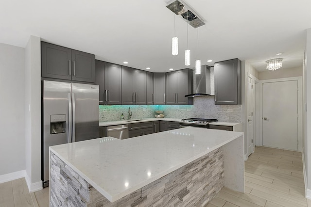 kitchen featuring light stone countertops, wall chimney range hood, decorative light fixtures, a kitchen island, and appliances with stainless steel finishes