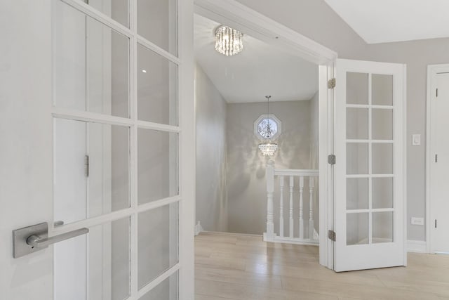 hallway featuring light hardwood / wood-style floors, lofted ceiling, and a notable chandelier