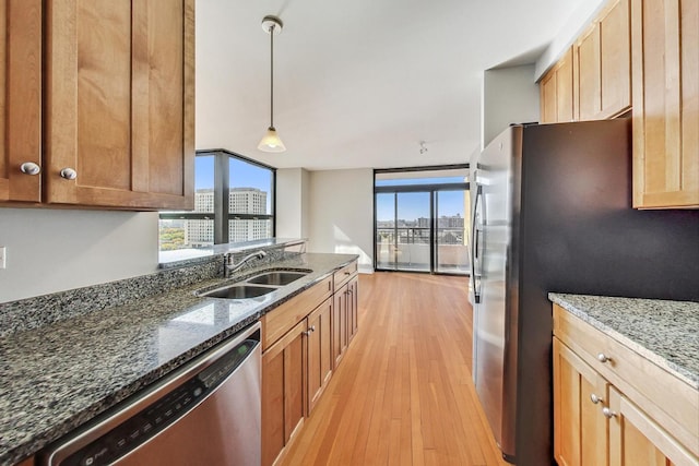 kitchen with dark stone counters, sink, light hardwood / wood-style flooring, appliances with stainless steel finishes, and decorative light fixtures