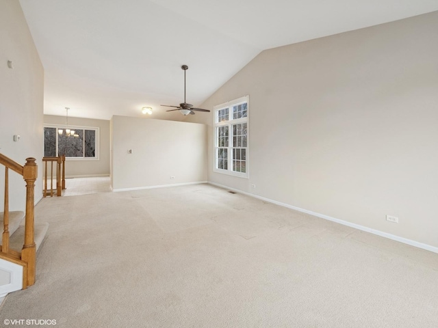 unfurnished living room with ceiling fan with notable chandelier, a healthy amount of sunlight, lofted ceiling, and light carpet