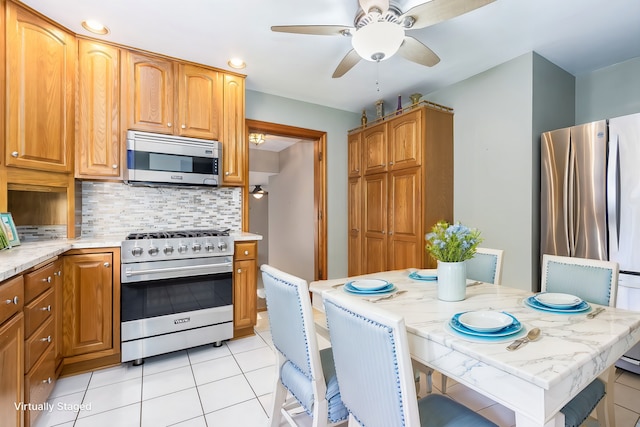 kitchen featuring backsplash, light stone counters, stainless steel appliances, ceiling fan, and light tile patterned floors