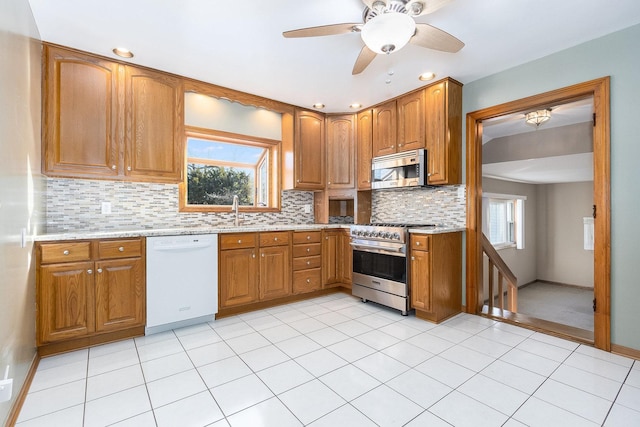 kitchen featuring decorative backsplash, appliances with stainless steel finishes, light stone countertops, a wealth of natural light, and ceiling fan