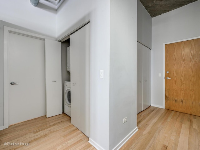 laundry area with stacked washer / dryer and light wood-type flooring