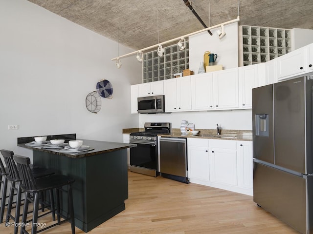 kitchen with a kitchen bar, stainless steel appliances, white cabinets, light hardwood / wood-style flooring, and sink