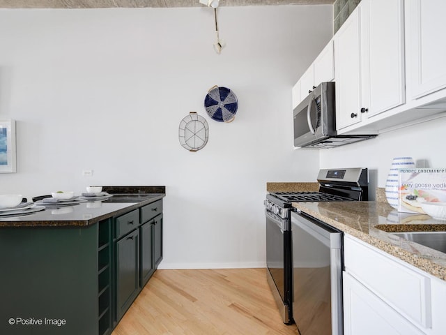 kitchen with white cabinetry, light hardwood / wood-style floors, green cabinets, appliances with stainless steel finishes, and dark stone counters