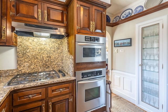 kitchen with light stone counters, tasteful backsplash, ornamental molding, and appliances with stainless steel finishes