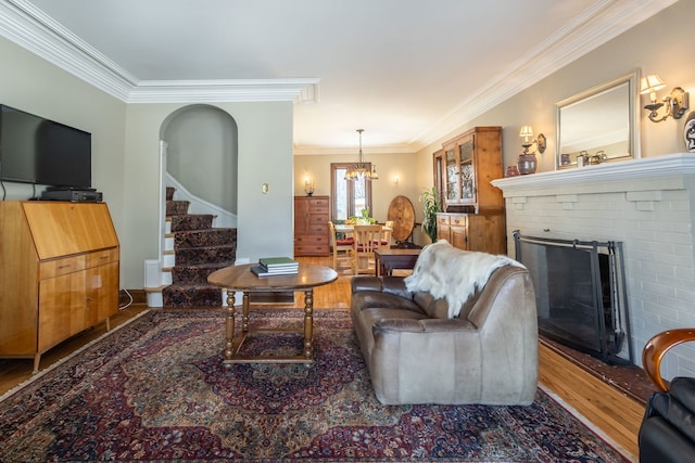 living room with a brick fireplace, crown molding, wood-type flooring, and a chandelier