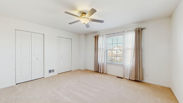 unfurnished bedroom featuring light carpet, two closets, and ceiling fan