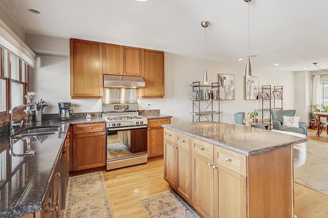 kitchen featuring stainless steel gas stove, sink, hanging light fixtures, a center island, and light wood-type flooring