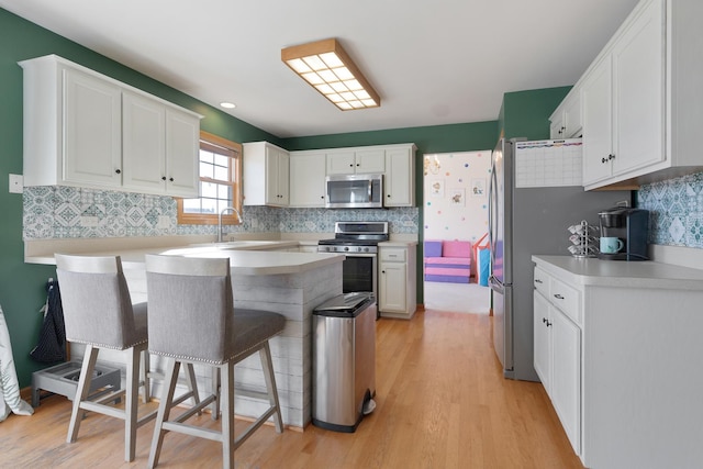 kitchen featuring a kitchen bar, appliances with stainless steel finishes, sink, light hardwood / wood-style flooring, and white cabinetry