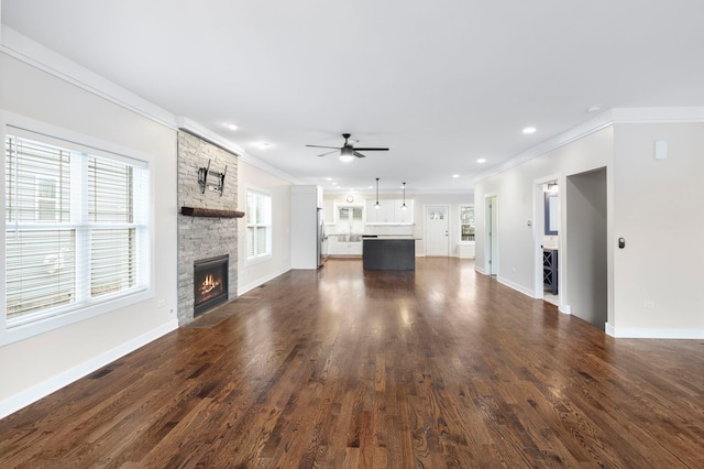 unfurnished living room with dark hardwood / wood-style floors, a stone fireplace, ceiling fan, and ornamental molding