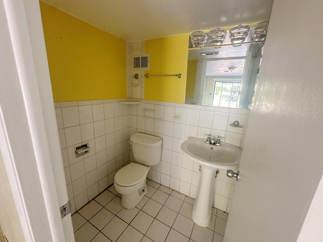 bathroom with toilet, tile patterned floors, and tile walls