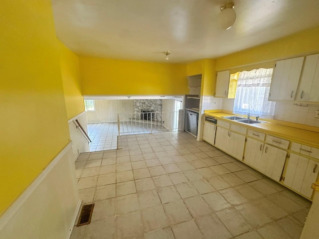 kitchen with backsplash, a stone fireplace, sink, and stainless steel dishwasher