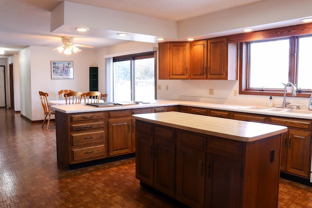 kitchen with a textured ceiling, a kitchen island, ceiling fan, and sink