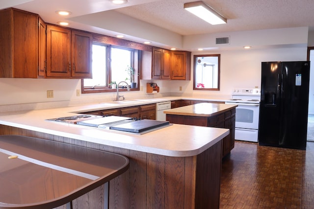 kitchen featuring a center island, white appliances, sink, a textured ceiling, and kitchen peninsula