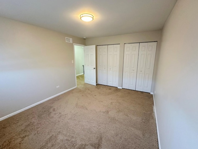 unfurnished bedroom featuring light colored carpet and multiple closets