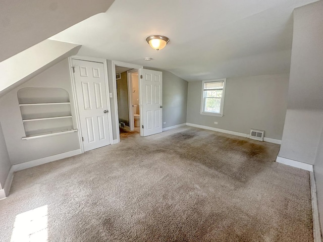 bonus room with built in shelves, carpet, and vaulted ceiling