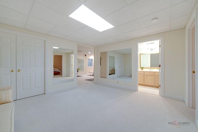 unfurnished bedroom with a paneled ceiling, a closet, light colored carpet, and ensuite bath