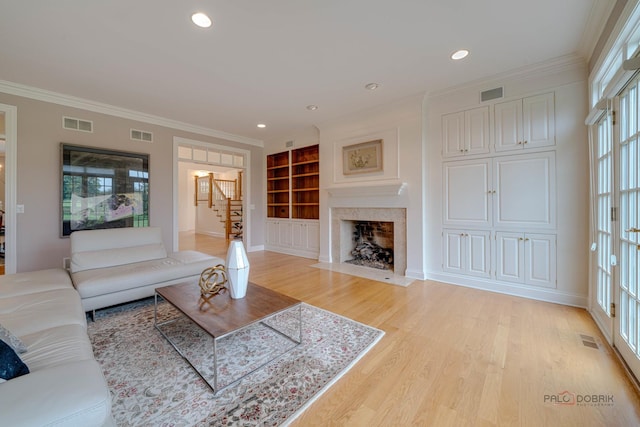 living room with a fireplace, built in shelves, light hardwood / wood-style floors, and crown molding